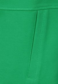 Tessuto verde con un aspetto tessuto e testurizzato. Presenta una cucitura verticale e una piccola tasca. Progettato per durabilità e funzionalità.