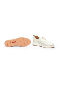 Zapatos blancos tipo slip-on con diseño perforado, plantilla acolchada y suela de goma con un fondo beige texturizado y acento rojo.