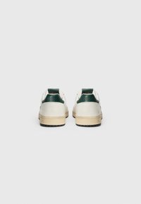 Ténis de couro branco com detalhes em verde e calcanhar texturizado. Notáveis pelo seu design de cano baixo e sola de borracha de goma com padrões de tracção.