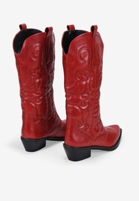 Botas de vaquero rojas de cuero con costuras decorativas, punta afilada y tacón bajo negro. Cuentan con tiradores para facilitar su puesta.