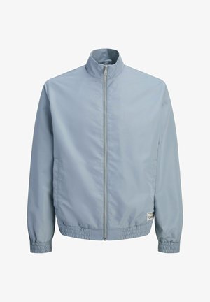 Veste zippée bleu clair avec col montant, poignets et ourlet élastiques, et deux poches latérales, présentée sur fond blanc.