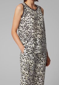 Květinový top bez rukávů na tmavém pozadí s bílými a žlutými kopretinami, s kulatým výstřihem a bočními kapsami.