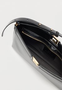 Μαύρη δερμάτινη τσάντα χειρός με λεία υφή, μεταλλικά στοιχεία σε χρυσαφί τόνο και κλείσιμο με φερμουάρ. Το εσωτερικό διαθέτει ύφασμα επένδυσης και θήκες οργάνωσης.