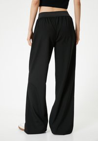 Zwarte wijde broek met een elastische tailleband, zachte stof, subtiele draping en geen zichtbare zakken. Glad textuur en een relaxed fit.