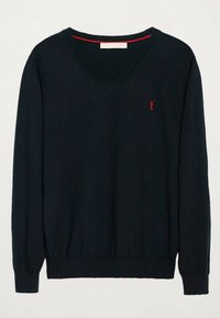 Pull en V bleu marine en tissu tricoté doux. Possède des poignets et un ourlet côtelés, avec un petit logo rouge brodé sur la poitrine.