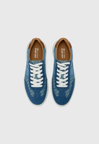Baskets en denim bleu avec des lacets blancs, des accents en cuir brun, des motifs texturés sur les côtés et une semelle en caoutchouc contrastée.