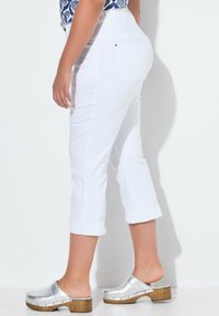 Pantalones cortos blancos con un diseño ajustado. Llevados con zuecos plateados. El material parece suave, con puños enrollados y detalles de costura mínimos.