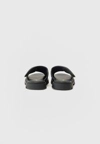 Black sandals with a flat sole, open back, and wide straps. Smooth texture with subtle inner detailing. Minimalist design, lightweight.