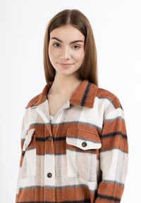 Camicia in flanella con motivo a quadri arancioni e bianchi, caratterizzata da due tasche sul petto, colletto e chiusura a bottoni. Tessuto morbido.