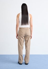 Béžové kalhoty s přímým střihem, s dvěma zadními kapsami a páskem v pase, vyrobené z hladké látky. Nošeny s bílým tílkem.