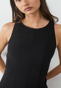 Schwarzes ärmelloses Kleid mit rundem Ausschnitt, charakterisiert durch vertikale Nähte und eine figurbetonte Silhouette, gefertigt aus einem glatten Stoff.