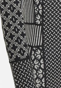 Strikkegenserarm med svarte og grå mønstre, inkludert geometriske design og striper; teksturert stoff; kontrasterende strikkedeler.