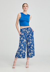 Top senza maniche blu abbinato a pantaloni a gamba larga con motivo floreale. I pantaloni presentano una vita elastica e tasche. Sandali bianchi con cinturino.