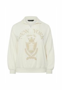 Felpa color crema con zip al colletto, caratterizzata da una grande grafica e un emblema "NEW YORK" in beige chiaro sul davanti.