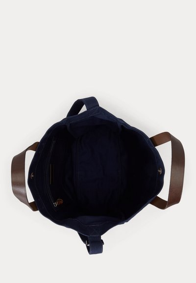 Toppvisning av en tom marineblå handlenett med brune lærhåndtak og en innerlomme med glidelås på en hvit bakgrunn.