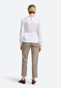 Witte blouse met lange mouwen, een peplum taille en een keyhole detail aan de achterkant, gecombineerd met beige broek met luipaardprint en donkere schoenen.