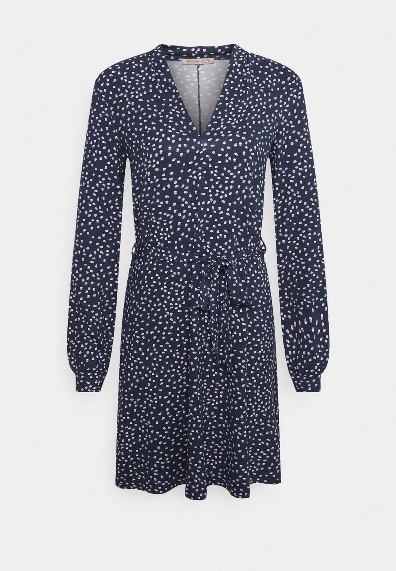 Mörkblå klänning med långa ärmar och omslagdesign. Har ett subtilt prickigt mönster i vitt och ljust rosa, med ett knyte i midjan.