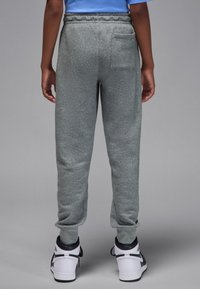 Hallid dressipüksid, millel on elastne vöökoht, kitsenevad sääred ja tagatasku. Kantud koos valgete ja mustade tossudega, millel on sile tekstuur.