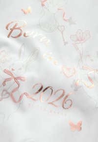 Biała tkanina z różowo-złotym tekstem "Urodzony w 2026 roku" oraz ilustracjami królików, kwiatów i motyli w pastelowych kolorach.