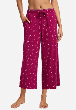 Woman wearing loose, cropped magenta pants with small white dandelion prints, an elastic waistband with a drawstring, and side pockets.