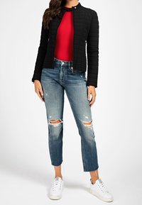 Giacca nera trapuntata con colletto alto, abbinata a un top rosso a coste e jeans blu strappati. Le sneakers bianche completano l'outfit.