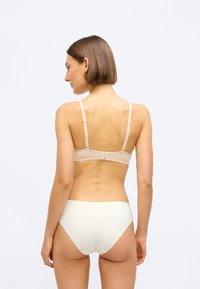 Bež grudnjak bez šavova s podešivim trakama i zatvaranjem na kuku, u kombinaciji s laganim kremastim gaćicama visokog struka, glatka tkanina, minimalni detalji.