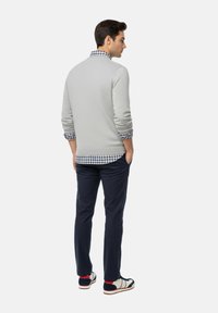 Suéter gris claro de tejido texturizado, superpuesto a una camisa de cuadros azul y blanca, combinado con pantalones oscuros de color marino y zapatillas blancas.