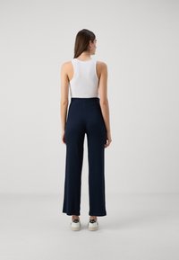 Navy, wide-leg pants with a high waist, made from smooth fabric. Paired with a white ribbed tank top and white sneakers with logo accent.