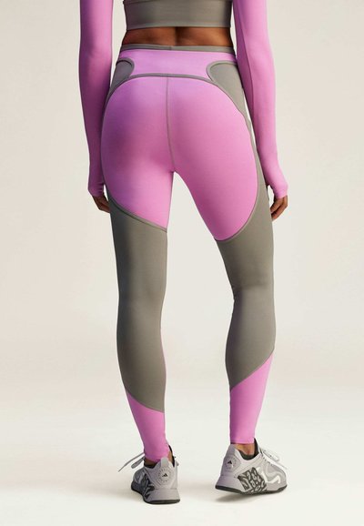 Leggings ajustados en gris y rosa con formas de panel contrastantes. El diseño presenta una textura sin costuras y una cintura alta, combinados con zapatos grises.