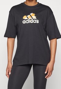Black oversized t-shirt with short sleeves, featuring a floral graphic and "adidas" logo in white and yellow on the front.