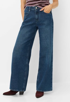 Femme portant un jean bleu foncé taille haute à jambes larges, un top rayé rentré et des bottines bordeaux à talons.