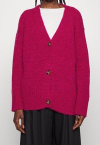 Fuchsie pletený cardigan s volným střihem, výstřihem do V a pěti knoflíky. Má žebrované manžety a lem, vyrobený z texturované příze.