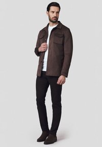 Brązowa zamszowa kurtka z kołnierzem, dwoma przednimi kieszeniami i zapięciem na guziki, w połączeniu z białą koszulą i czarnymi spodniami. Gładka tekstura.