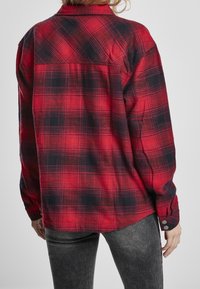 Rød og sort plaid skjorte med lange ærmer, knapmanchetter og en afslappet pasform. Fremstillet af et blødt, tekstureret stof med en buet kant.