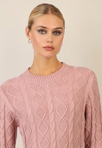Jasnoróżowy sweter o fakturowanej strukturze z wzorem w warkocze, z ribbowanym dekoltem i dopasowanym krojem.