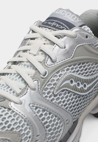 Κοντινό πλάνο λευκού και γκρι παπουτσιού τρεξίματος Saucony Triumph με επάνω μέρος από διχτυωτό υλικό, συνθετικές επικαλύψεις και ασφαλιστικά κορδόνια.