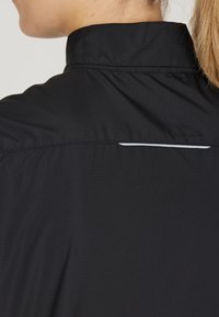Schwarzes Hemd aus strukturiertem Stoff, mit Stehkragen und einem weißen Akzentdetail auf der Rückseite. Entworfen im schlanken, minimalistischen Stil.