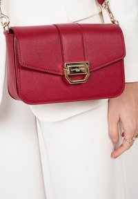 Borsa a tracolla rossa in pelle con chiusura a patta, hardware dorato e logo in rilievo. Presenta una superficie texturizzata e una tracolla in catena regolabile.