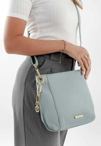 Borsa a tracolla in pelle azzurro chiaro con finitura texturizzata, dettagli in metallo dorato e forma rettangolare. C'è una tracolla regolabile attaccata.