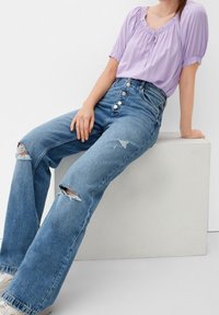 Light purple short-sleeve blouse with a ruffled neckline paired with high-waisted blue denim jeans featuring distressed knees and five buttons.