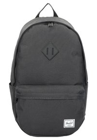 Mochila de tela negra con una textura suave, parche en forma de diamante, bolsillo frontal con cremallera y etiqueta de marca blanca en la parte inferior frontal.