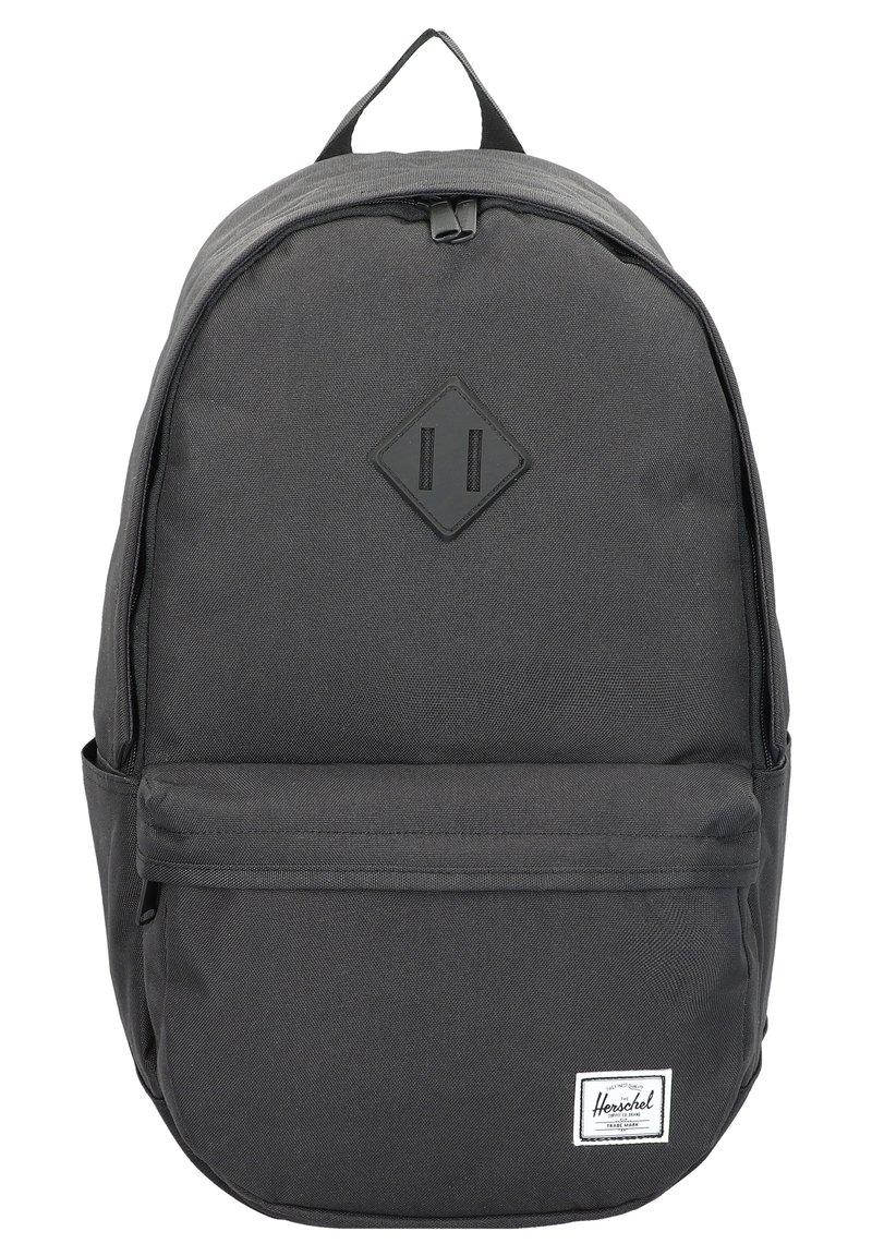 Mochila de tela negra con una textura suave, parche en forma de diamante, bolsillo frontal con cremallera y etiqueta de marca blanca en la parte inferior frontal.