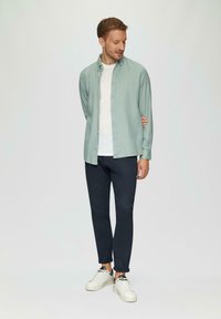 Licht blauwe button-up shirt over een wit T-shirt, gedragen met donkerblauwe broek en witte sneakers. Zachte stof met een relaxte pasvorm.