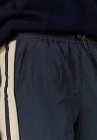 Tengerészeti sportnadrág könnyű anyagból; rugalmas derékpánttal, zsinórral és krémszínű függőleges csíkokkal az oldalán.