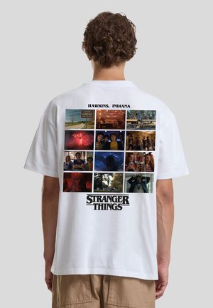 Weißes T-Shirt mit einer Collage von Szenen aus "Stranger Things" auf der Rückseite, darüber der Titel und "Hawkins, Indiana" gedruckt.
