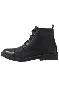 Botas de tobillo de cuero negro con un acabado texturizado, punta redonda, diseño de cordones, costuras en contraste y un pequeño logo en el lateral.