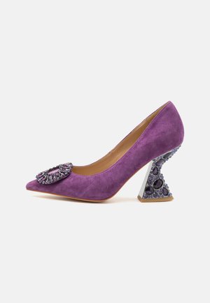Tacco alto in suede viola con punta affusolata e dettaglio floreale decorato. Il tacco scultoreo presenta gemme viola e un design triangolare.