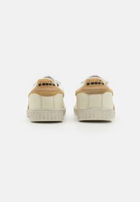 Hvite lær sneakers med beige semsket skinn-detaljer, teksturerte gummisåler og svart logo på hælen. Rund tå og lavprofil design.
