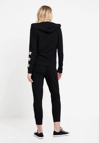 Sudadera negra con estrellas en las mangas, fabricada en un tejido suave. Combinada con pantalones de chándal negros a juego. Look casual, con un ajuste relajado y capucha.