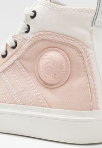 Vysoké tenisky s tělem z bledě růžové plátěné látky, bílými detaily, černými průramky a gumovou podrážkou. Obsahují strukturovanou růžovou nášivku s logem.